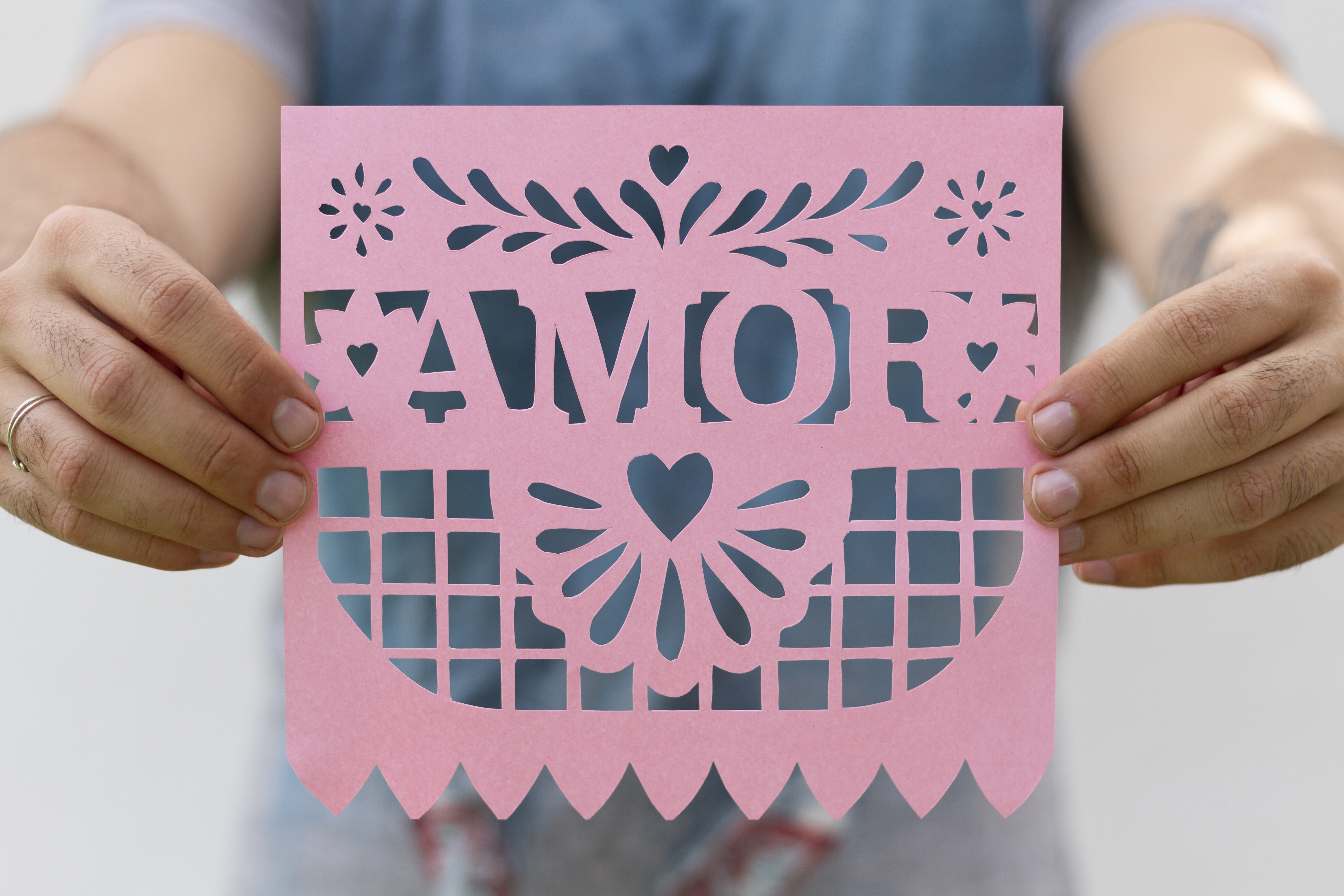 Mãos segurando uma peça de papel rosa com a palavra Amor e detalhes recortados